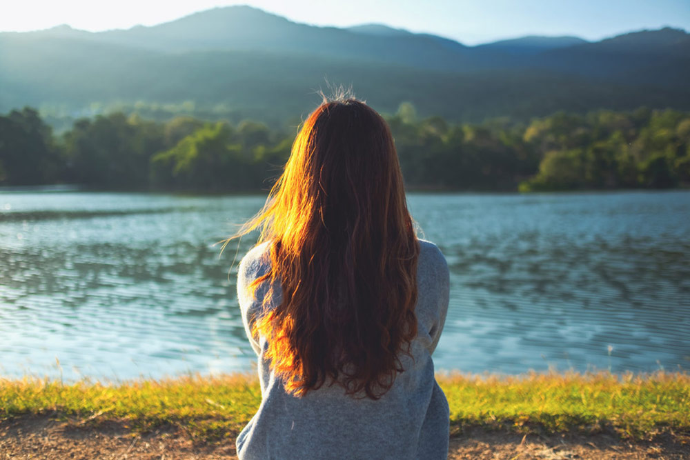 Chica sentada sola frente a un lago representando la tristeza